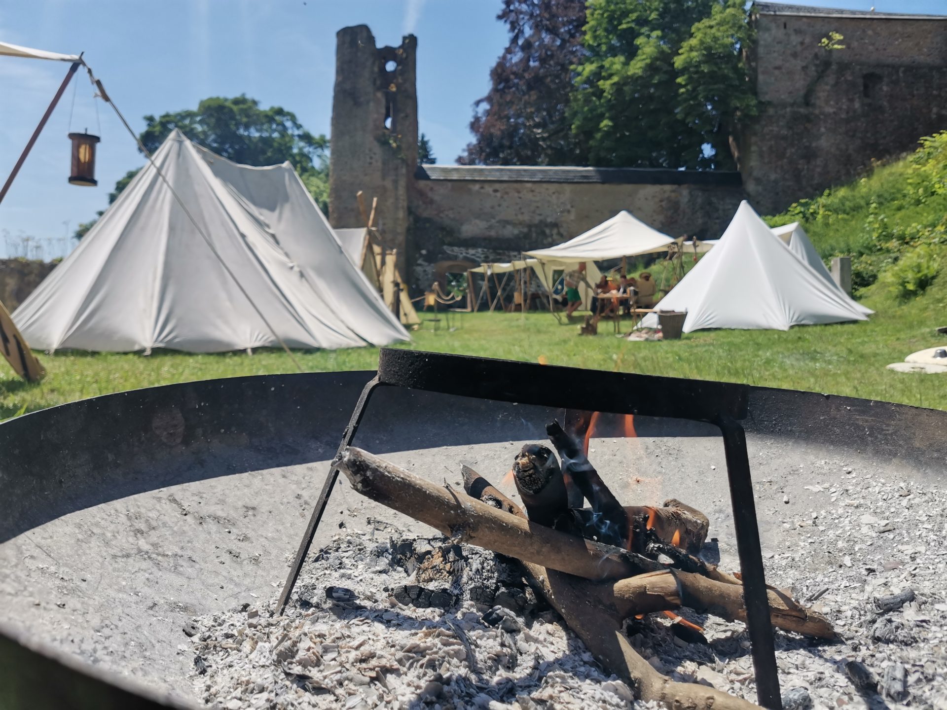 Lagerfeuer im Vordergrund, dahinter Zelte und Teilnehmer im Burghof