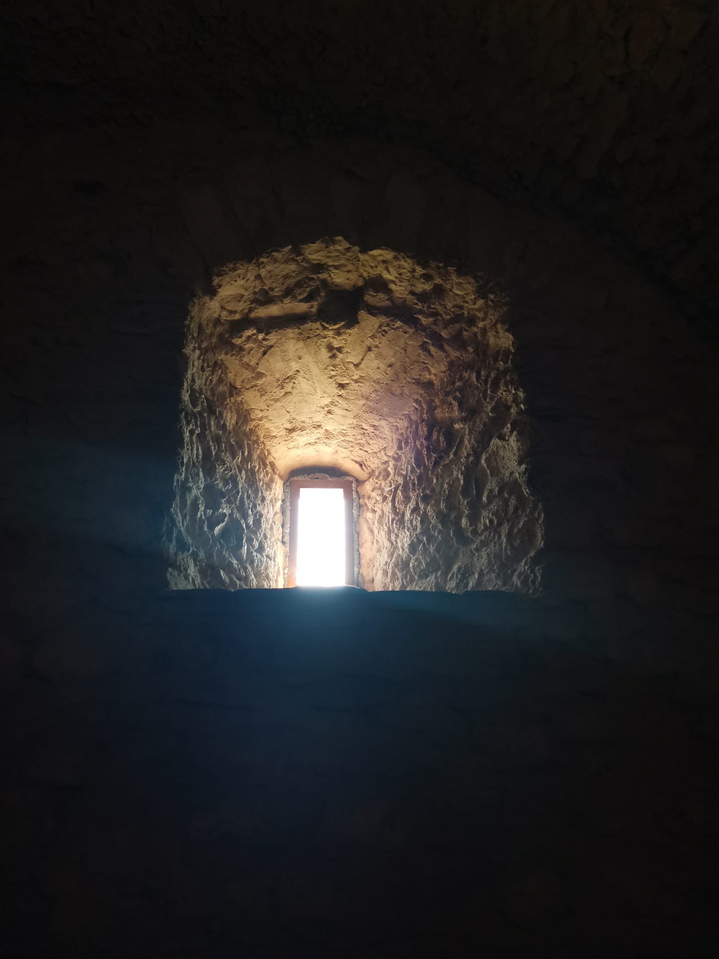 Schmales Bogenfenster in einer mittelalterlichen Burgmauer, helles Licht strahlt durch den dunklen Steinrahmen