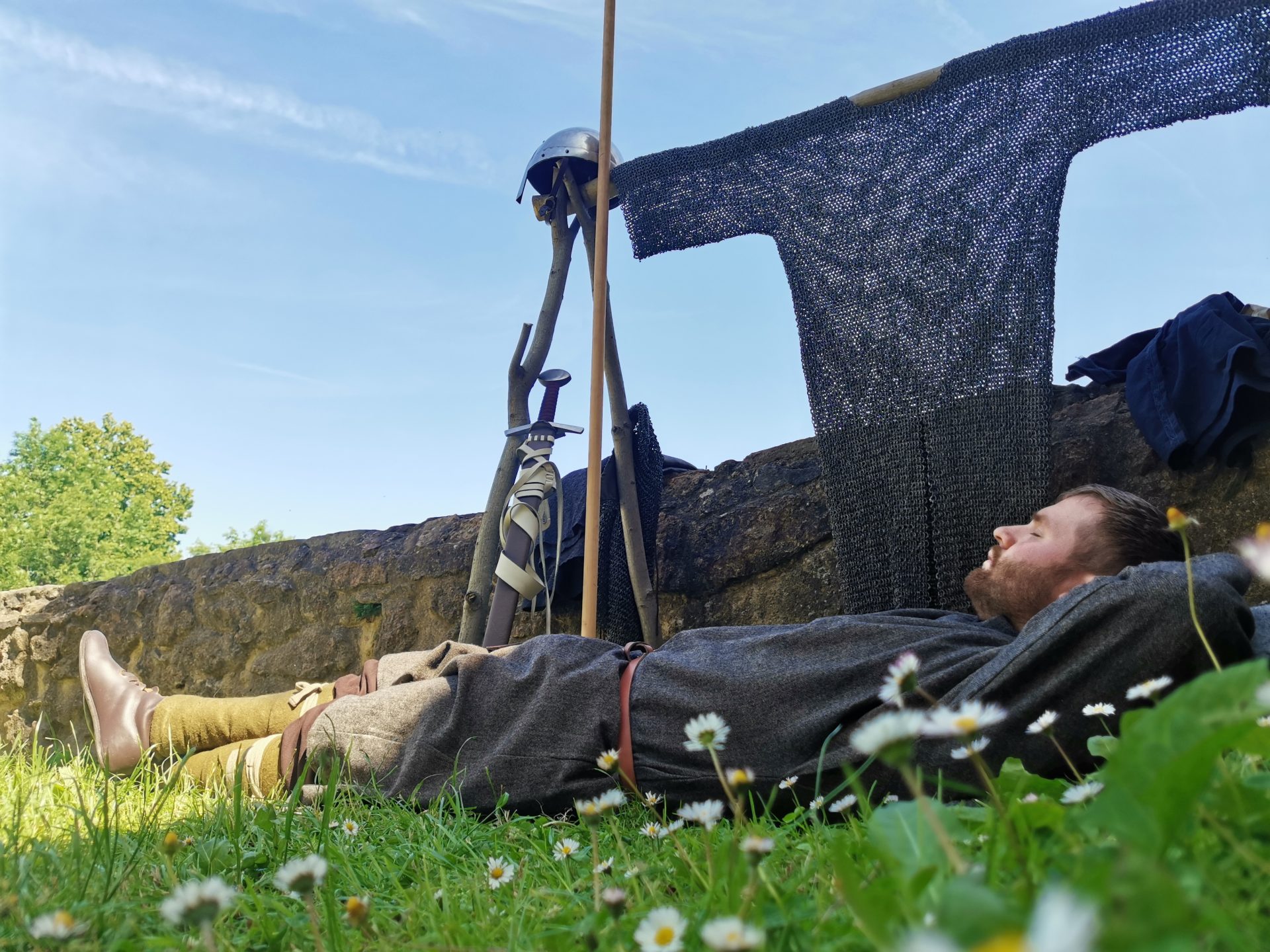 Darsteller ruht in der Mittagspause im Gras neben Helm, Schwert und Kettenhemd