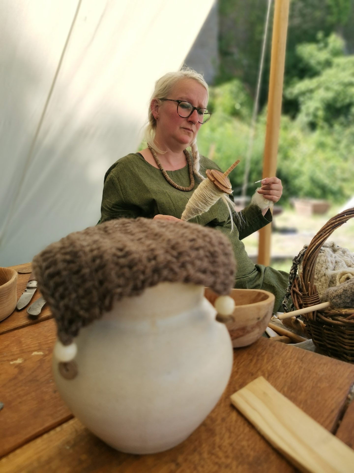 Frau in mittelalterlichem Gewand spinnt Wolle mit einer Handspindel in einem Zelt